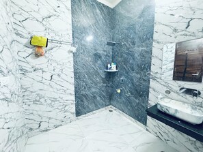 A bathroom with a marble floor, a black marble shower wall, a yellow cleaning cloth, a shelf with toiletries, and a sink with a mirror.