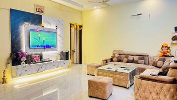 A modern living room with a marble floor, a large flat-screen TV, a sofa, a coffee table, and a ceiling fan.