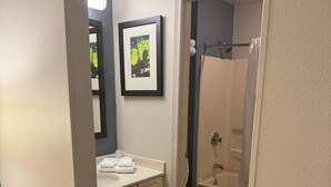 A bathroom with a toilet, sink, and shower area. There are framed pictures on the wall and a towel rack.
