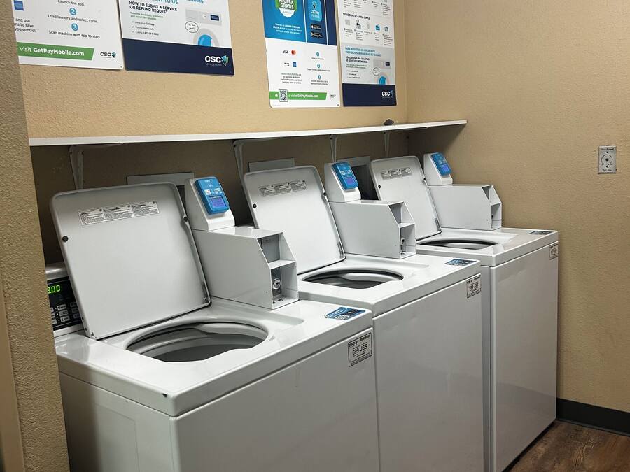 A laundromat with four washing machines and instructional posters on the wall.