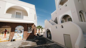 A courtyard with white buildings, stone walls, and a clear blue sky. - Blue Arise Fira (Santorini)