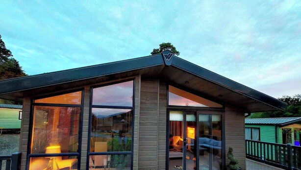 Une maison moderne dotée de grandes baies vitrées, d’une terrasse en bois et d’un toit végétalisé.