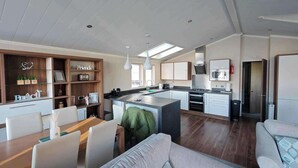 Une cuisine moderne dotée d’un îlot central, de meubles blancs et d’un coin repas avec une table et des chaises en bois.