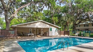 A swimming pool with a covered seating area, surrounded by trees and a fence.
