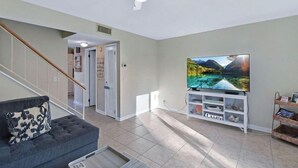 A living room with a flat-screen TV, a grey sofa, and a ceiling fan.
