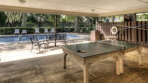 An outdoor pool area with a ping pong table, lounge chairs, and a covered seating area.