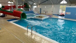 Una piscina interior con tobogán de agua, plataforma de salto y puesto de socorrista.