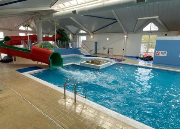 Una piscina al coperto con uno scivolo acquatico, una piattaforma tuffatori e un posto di salvataggio.