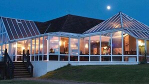 Un edificio amplio con techo de vidrio y tejado inclinado, probablemente un restaurante o espacio para eventos, con una escalera que conduce a la entrada.