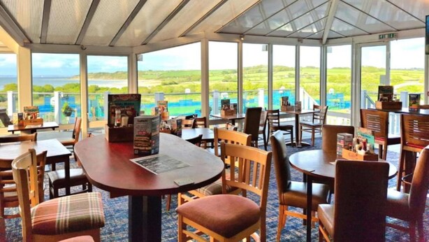 Un restaurante con mesas y sillas, grandes ventanales y vistas al paisaje.