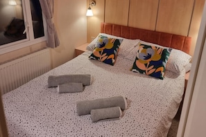A neatly made bed with floral pillows, a patterned bedspread, and two rolled towels. - Free Ferry on 7 Days Bookings Jul/aug (Cowes)