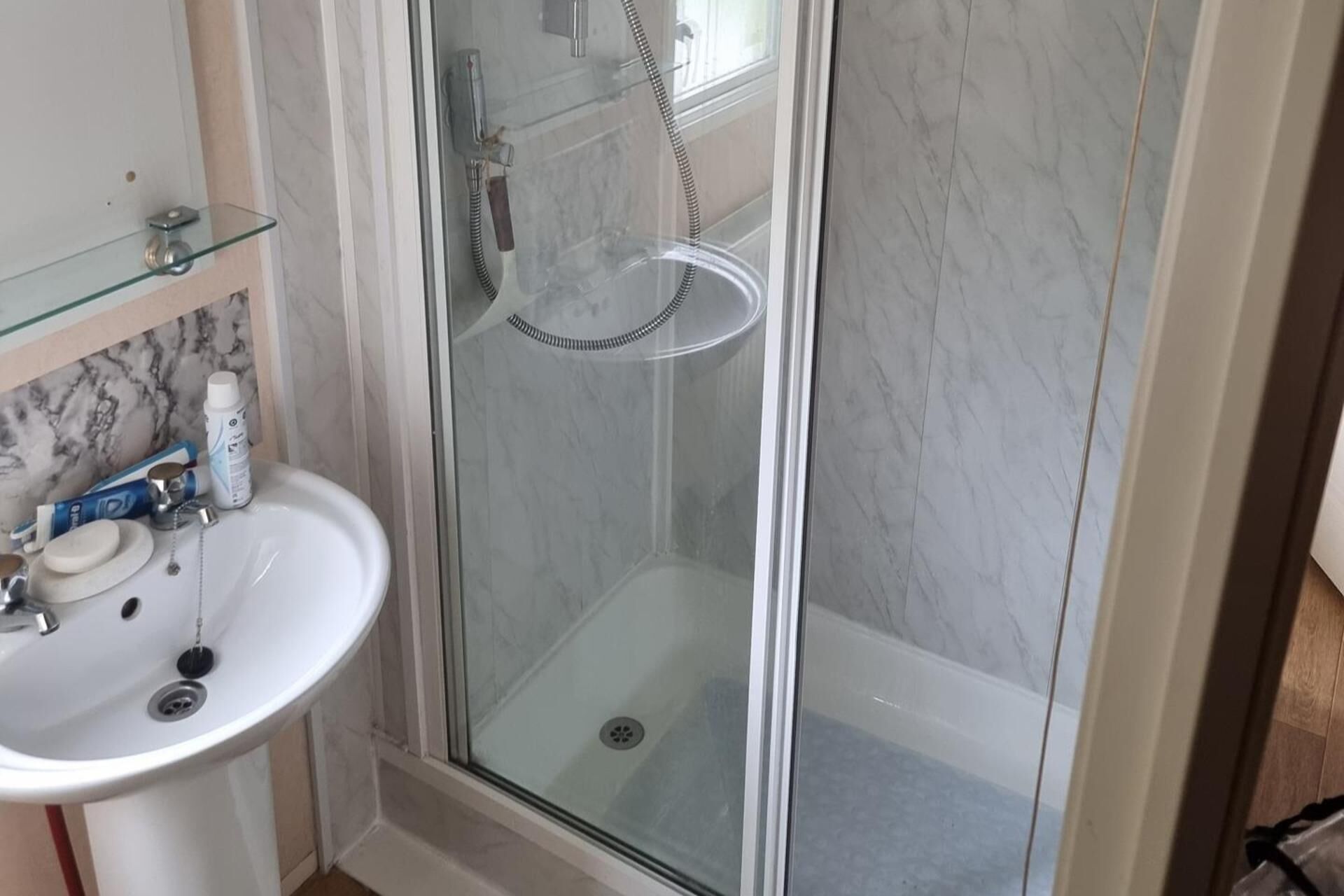 A bathroom with a glass-enclosed shower, a white sink, and a marble backsplash.