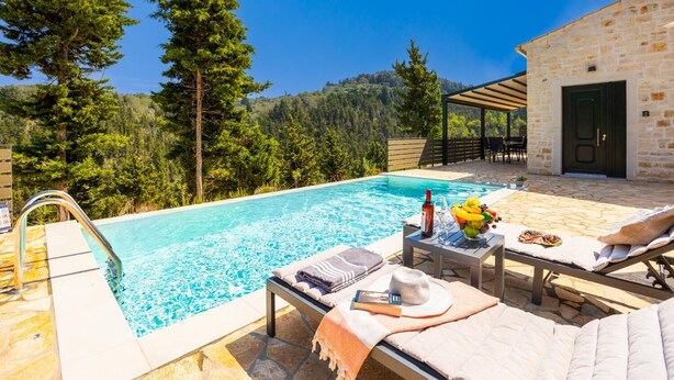 Zona de piscina con edificio de piedra, sillas de descanso y una mesa con una botella y fruta.