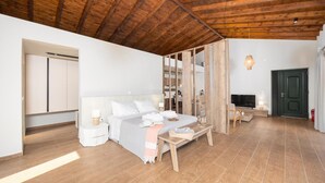 Un dormitorio moderno con techo de madera, una cama con ropa blanca, una mesita de noche con lámpara y un televisor.