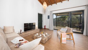 Un salón moderno con un televisor de pantalla plana, muebles de madera y un amplio ventanal corredero a un balcón.