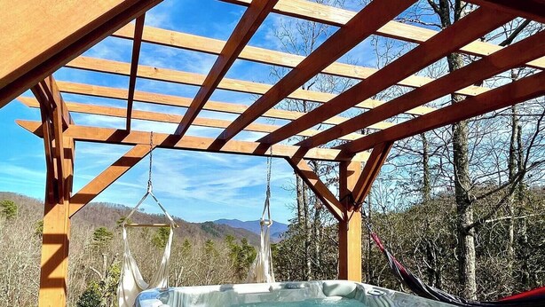 Un jacuzzi bajo una pérgola de madera con montañas al fondo.
