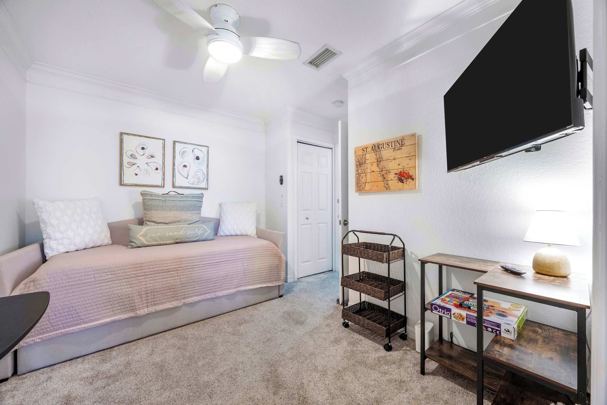 A bedroom with a bed, a wall-mounted TV, a ceiling fan, and a small table with a lamp.