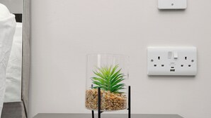 Ein klarer Glas-Pflanzgefäß mit Pflanze auf einem Tisch, eine weiße Wand und eine Steckdose.