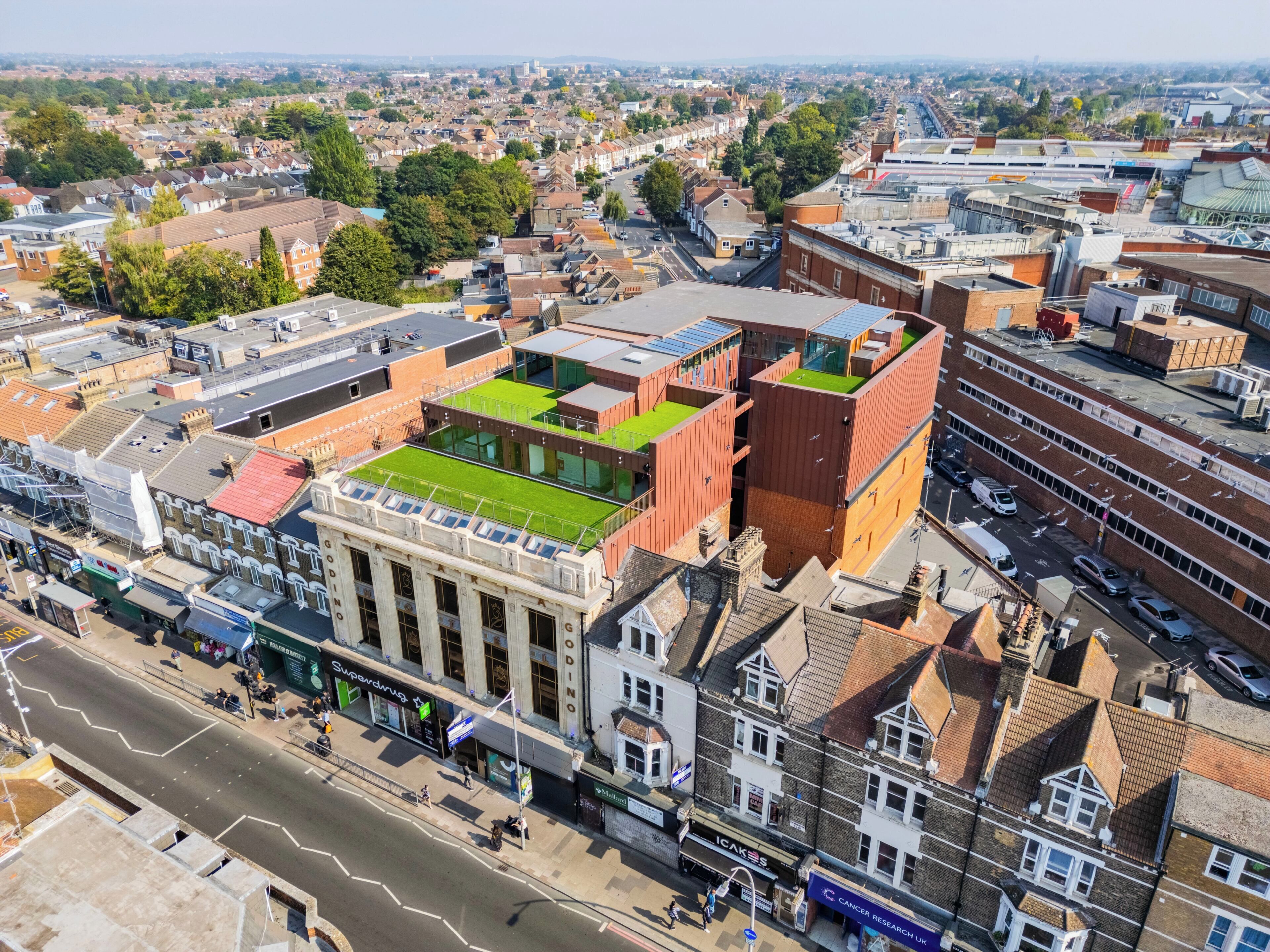 Une vue aérienne d’une ville, avec un mélange de bâtiments résidentiels et commerciaux, dont un bâtiment remarquable doté d’un toit végétalisé et d’une façade de style classique.
