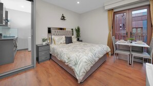 A modern bedroom with a large bed, a small table, and a chair. There is a sliding door leading to a balcony.