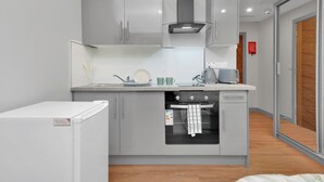 A compact kitchen with grey cabinets, a built-in oven, and a small refrigerator.