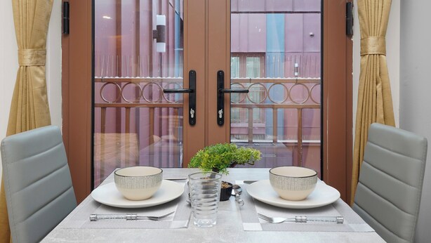 A dining table set with two bowls, a glass, and cutlery, with a small plant in the center.