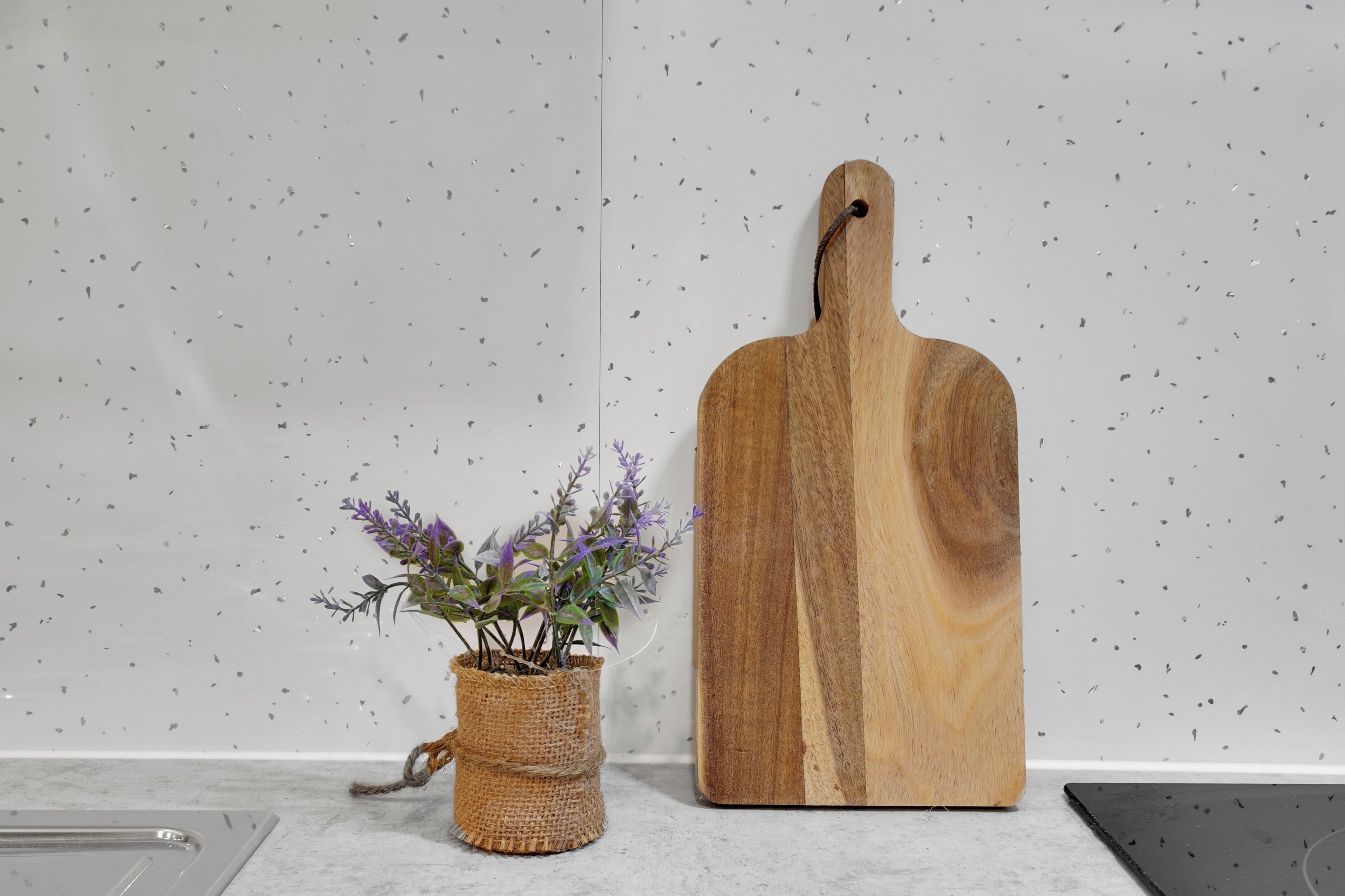 Een houten snijplank en een rieten mand met een plantje op een aanrecht.