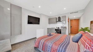 Un dormitorio moderno con una cama grande, una pequeña kitchenette y un televisor montado en la pared.