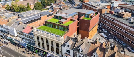 An aerial view of a cityscape with a mix of residential and commercial buildings, including a prominent building with a green roof and a classical facade.