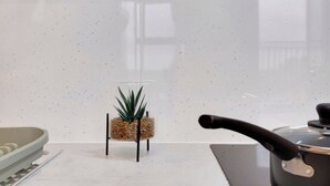 Una cocina con salpicadero blanco moteado, una planta pequeña en maceta sobre un soporte negro, y un hervidor en la encimera.