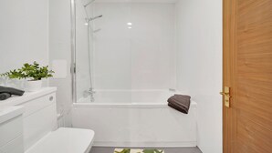 Une salle de bain moderne avec une douche à parois de verre, un lavabo blanc et une porte en bois.