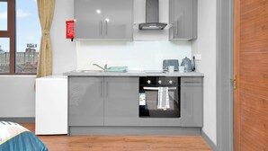 Une cuisine moderne avec des meubles gris, un four encastré et une fenêtre donnant sur des immeubles.