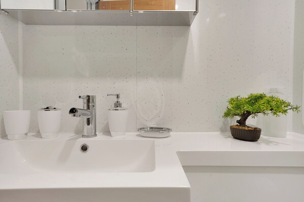 A modern bathroom with a white sink, two white cups, a soap dispenser, and a small potted plant.