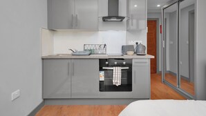 A compact kitchen with grey cabinets, a built-in oven, and a small countertop. - London City Apartment in Ilford (Ilford)