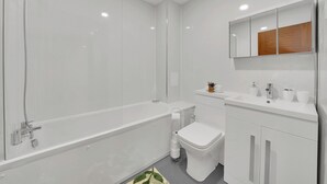 A modern bathroom with a bathtub, toilet, and sink. - London City Apartment in Ilford (Ilford)