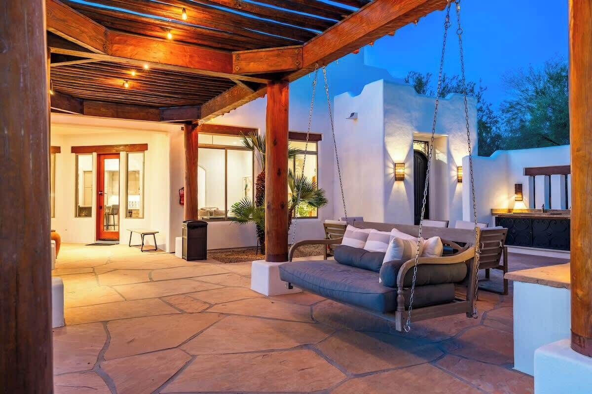 An outdoor patio with a swing, a stone floor, and a covered area with a wooden ceiling.