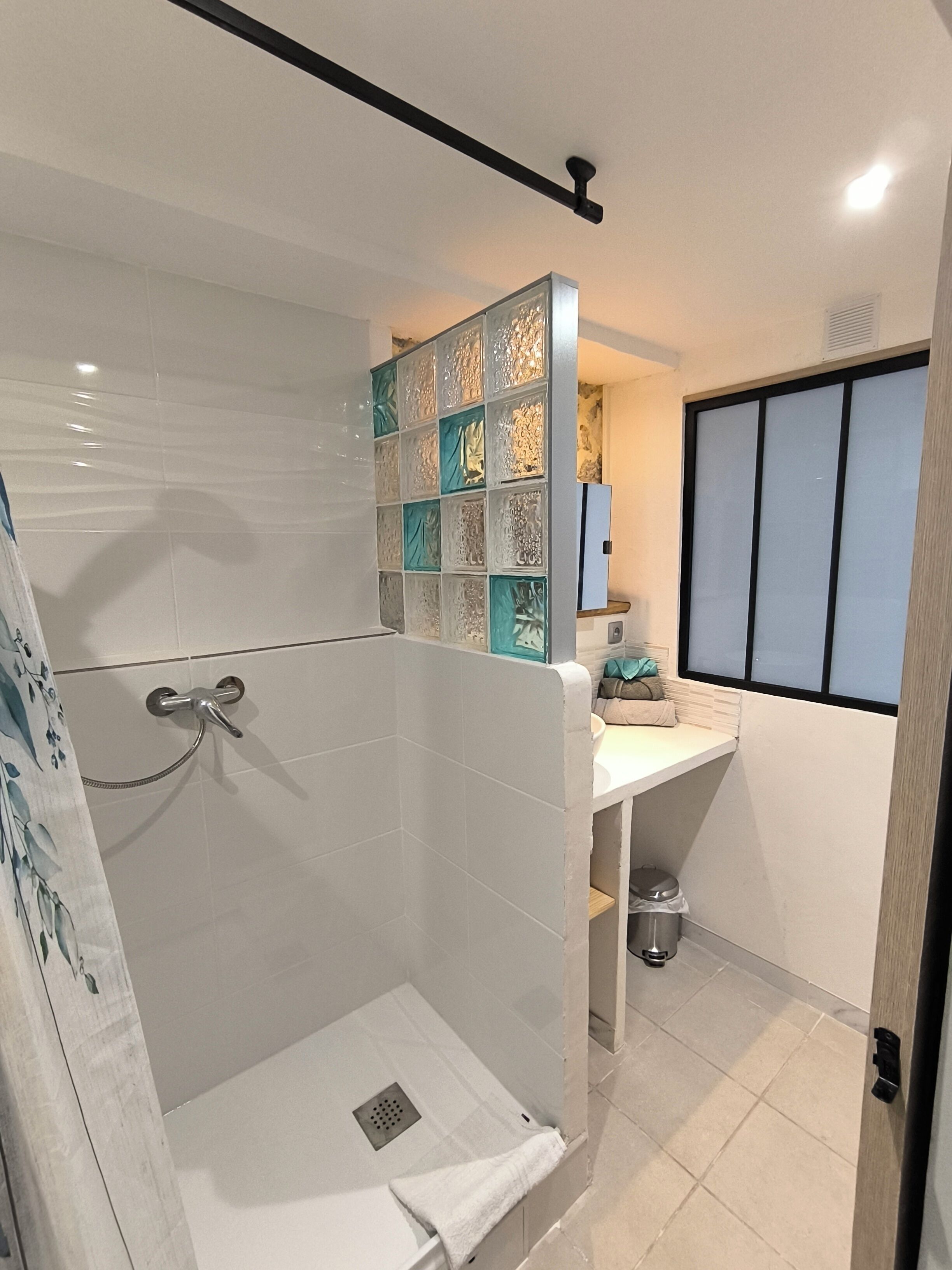 Un baño moderno con cabina de ducha de vidrio, un lavamanos blanco y un respuesto de azulejos decorativos.