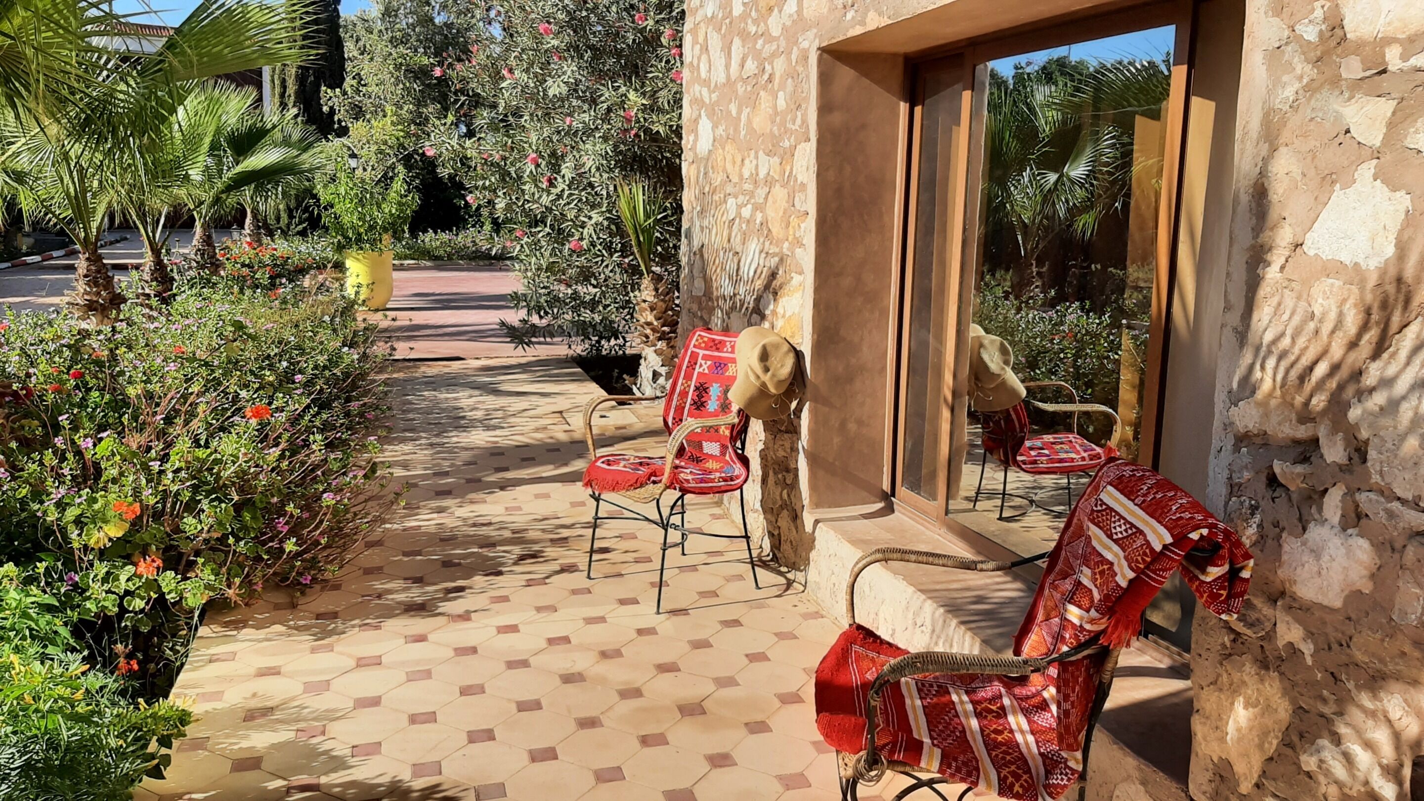 Un patio con suelo de baldosas hexagonales, mobiliario exterior con cojines rojos y una pared de piedra.