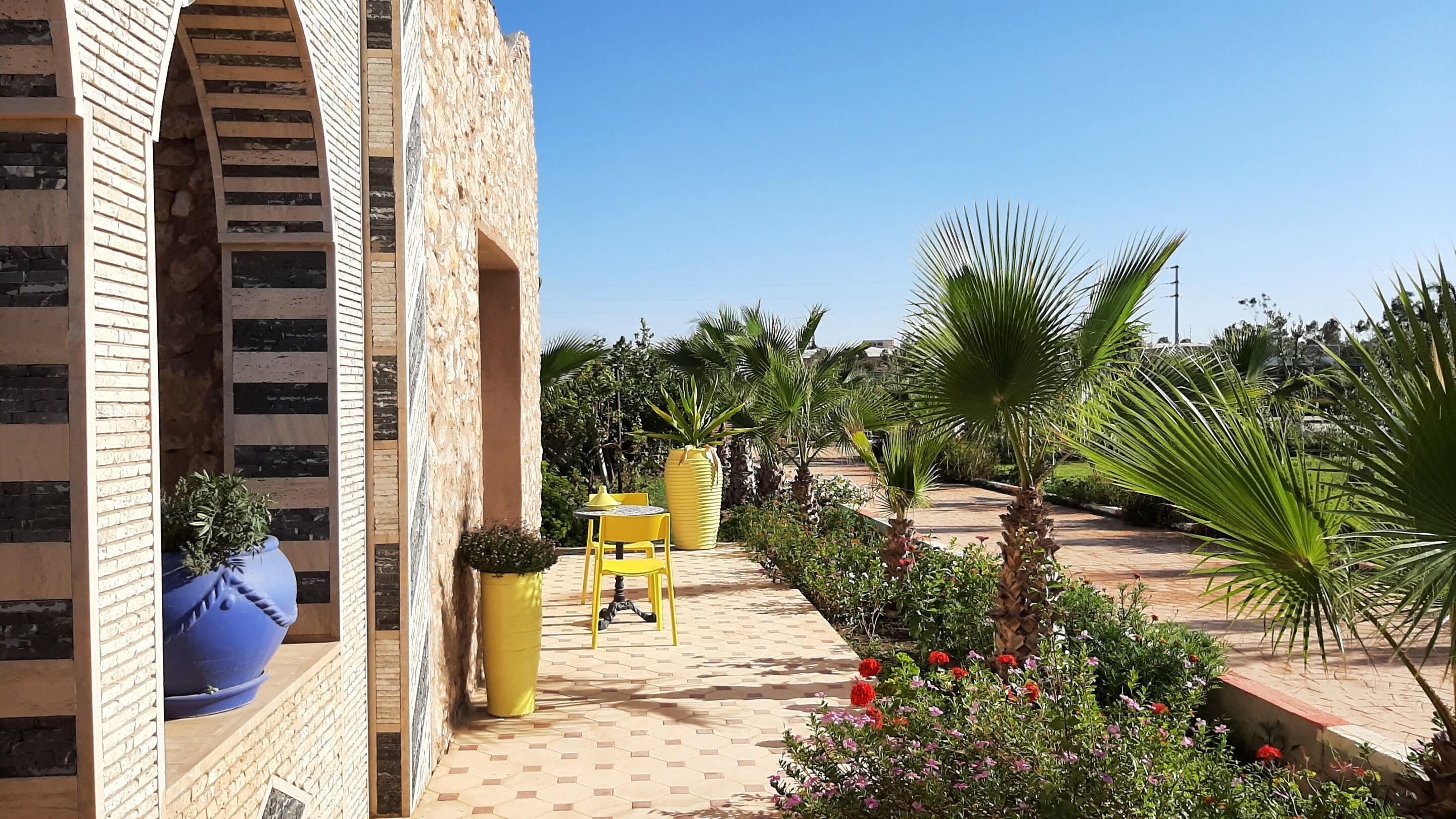 Une cour avec un bâtiment en briques, des chaises jaunes et des plantes en pot.