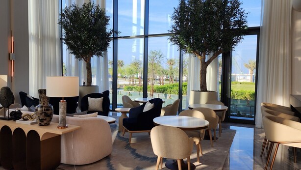 Eine moderne Lounge mit runden Tischen, bequemen Sitzgelegenheiten und zwei großen Bäumen.