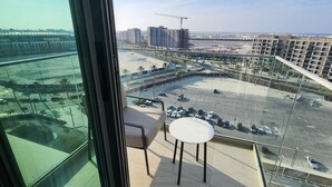 Ein Hotelzimmer in einem Hochhaus mit großem Fenster und Blick auf einen Parkplatz, einen Strand und umliegende Gebäude.