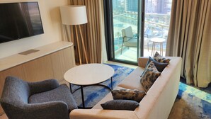 Ein Hotelzimmer mit Sofa, Sessel, rundem Tisch und einem an der Wand befestigten Fernseher.