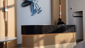 Ein moderner Empfangsbereich mit einer Marmor-Rezeption, einem an der Wand befestigten abstrakten Kunstwerk und einer Sitzecke mit rundem Tisch.