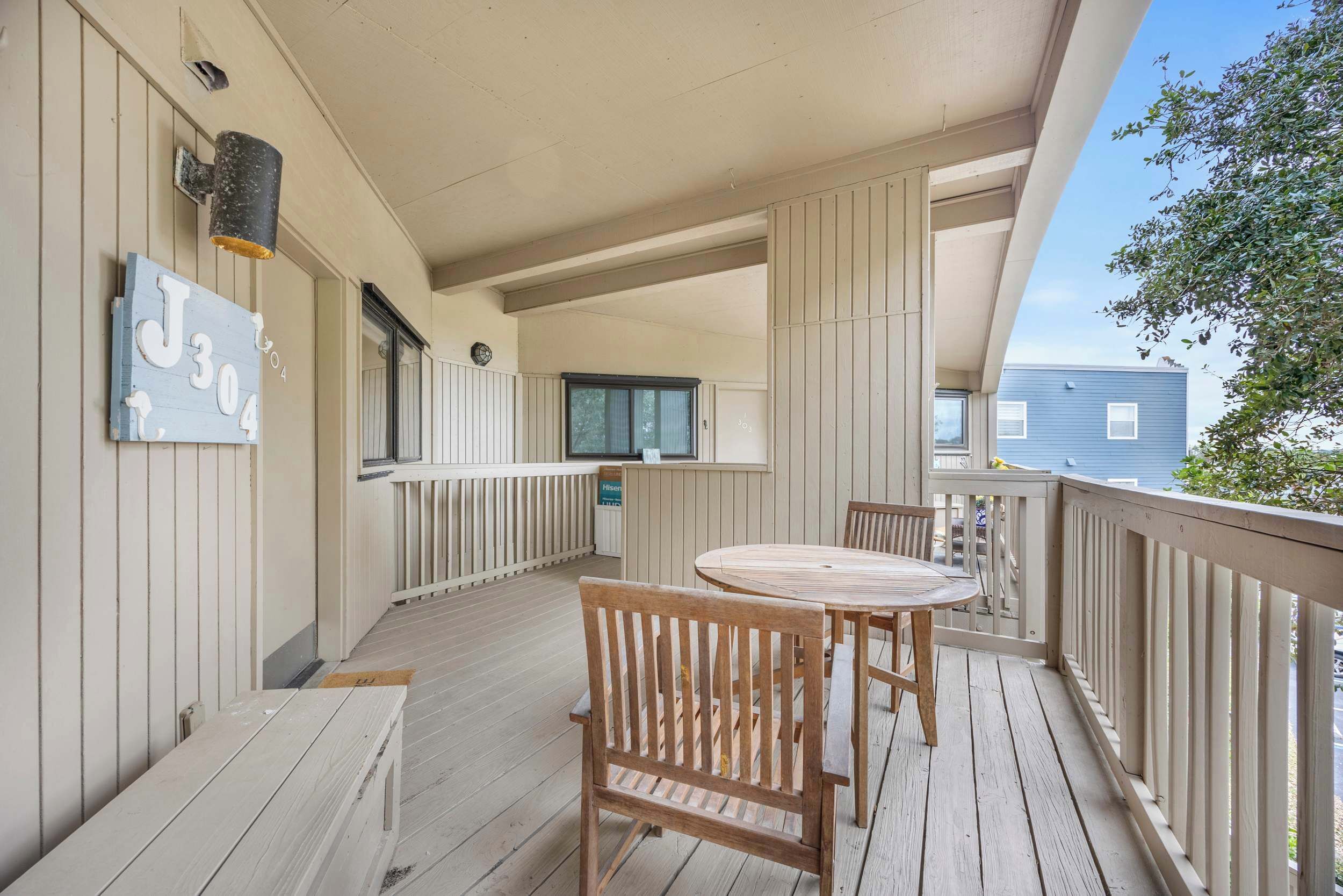 A wooden deck with a round table and chairs, a sign with numbers, and a window.