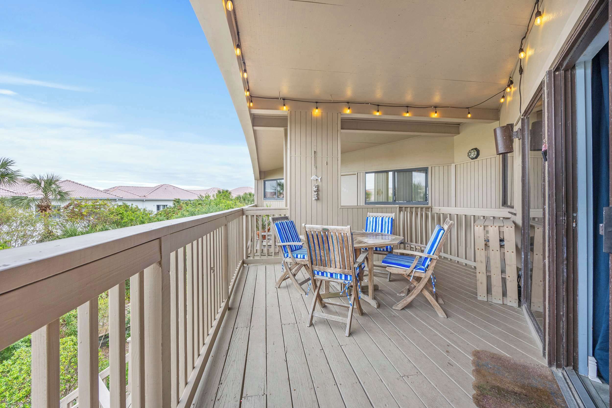 A wooden deck with a table and chairs, a railing, and string lights.