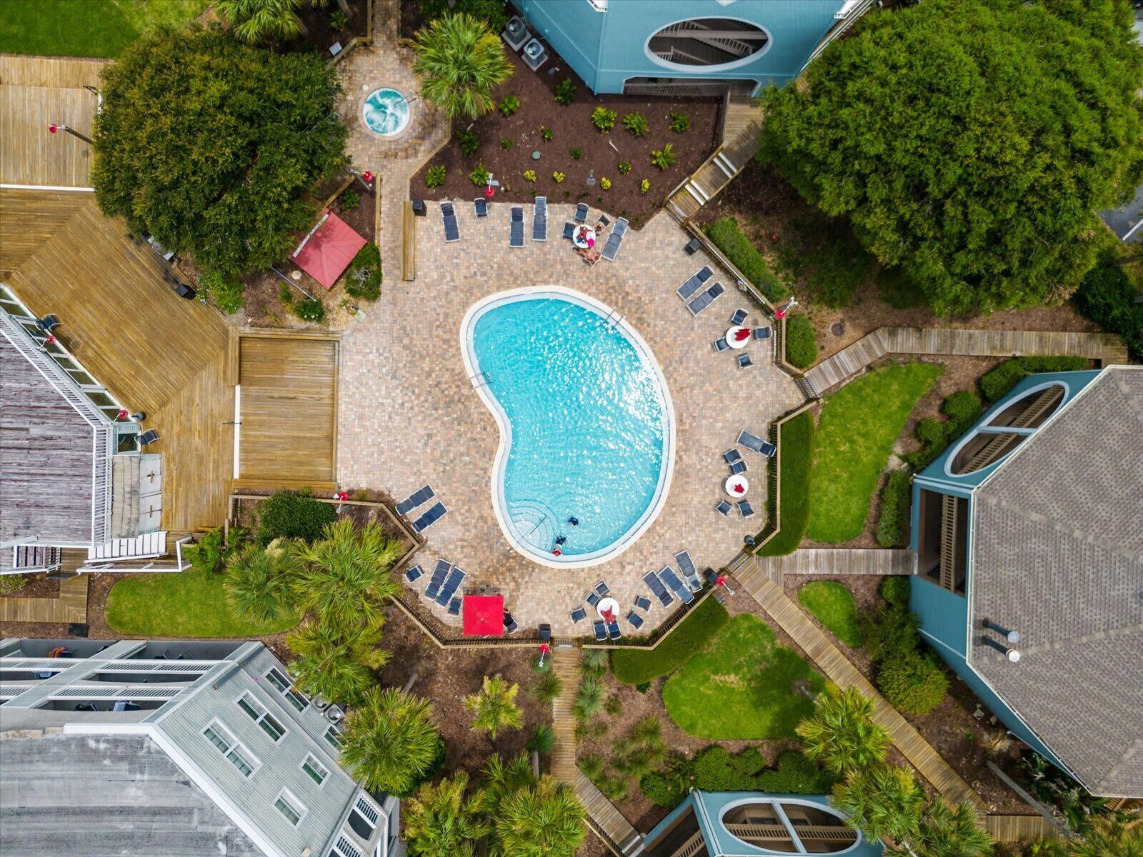 An aerial view of a backyard with a swimming pool, sun loungers, and a small hot tub.