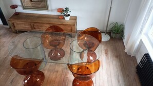 A dining area with a glass-top table and orange chairs, a wooden bench, a floor lamp, and a mirror on the wall.