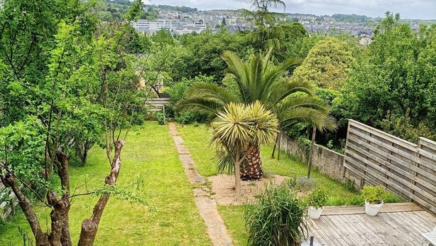 A garden with a wooden deck, a pathway, and a view of a town in the distance.