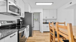 A modern kitchen with stainless steel appliances, white cabinets, and a wooden dining table.