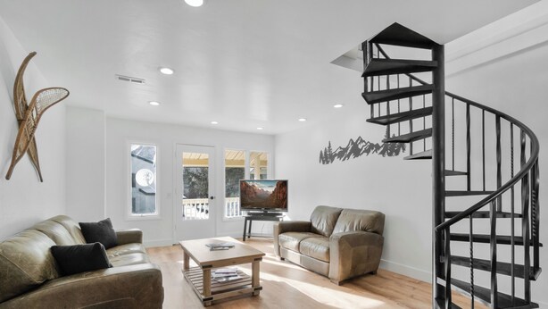 A modern living room with a spiral staircase, leather sofas, a wooden coffee table, and a TV.